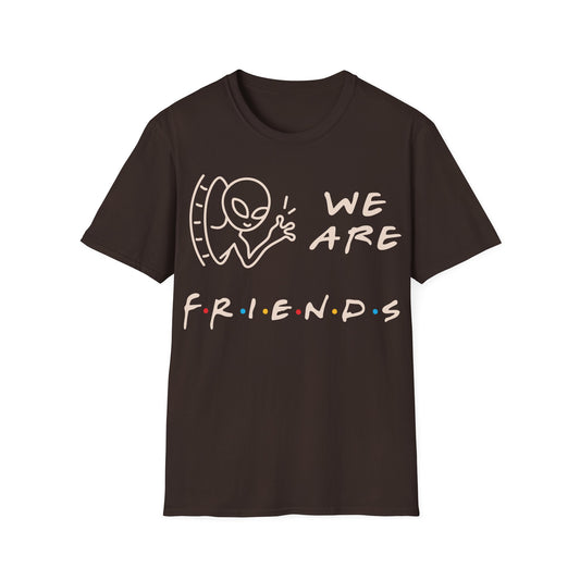 We Are Friends t-shirt design, featuring a smiling alien waving through a doorway beside playful handwritten lettering with colorful dot accents on a dark chocolate background