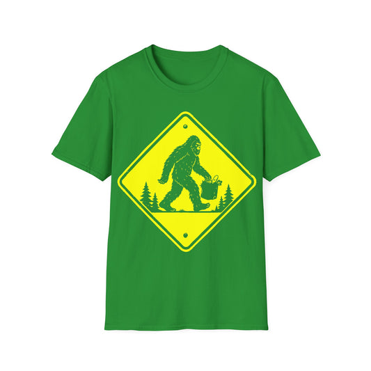 Bigfoot Road Sign t-shirt design, featuring a black Sasquatch carrying a grocery bag through a pine forest on a bright diamond-shaped warning sign on an irish green background